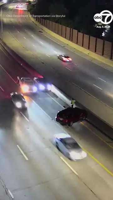 A person standing outside of his broken down car on the shoulder of a busy highw