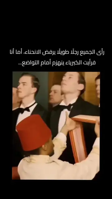 يرفع رجل يرتدي طربوشًا أحمر وشاحًا برتقاليًا وكريمي اللون أمام صف من الرجال الذي